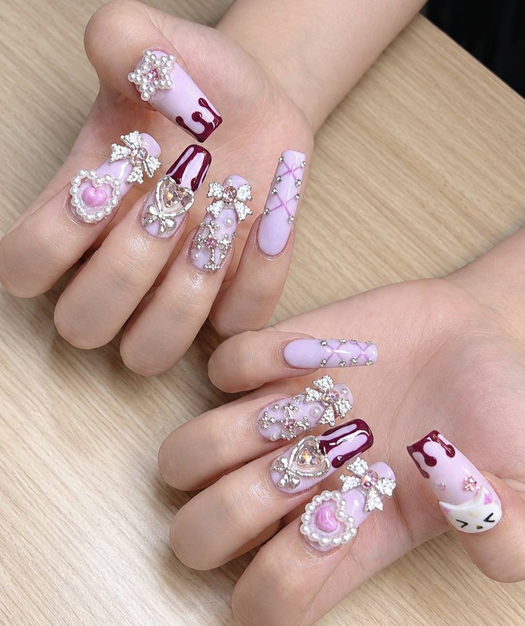 Long lilac nails with pearl and crystal hearts, jeweled bows and burgundy accents